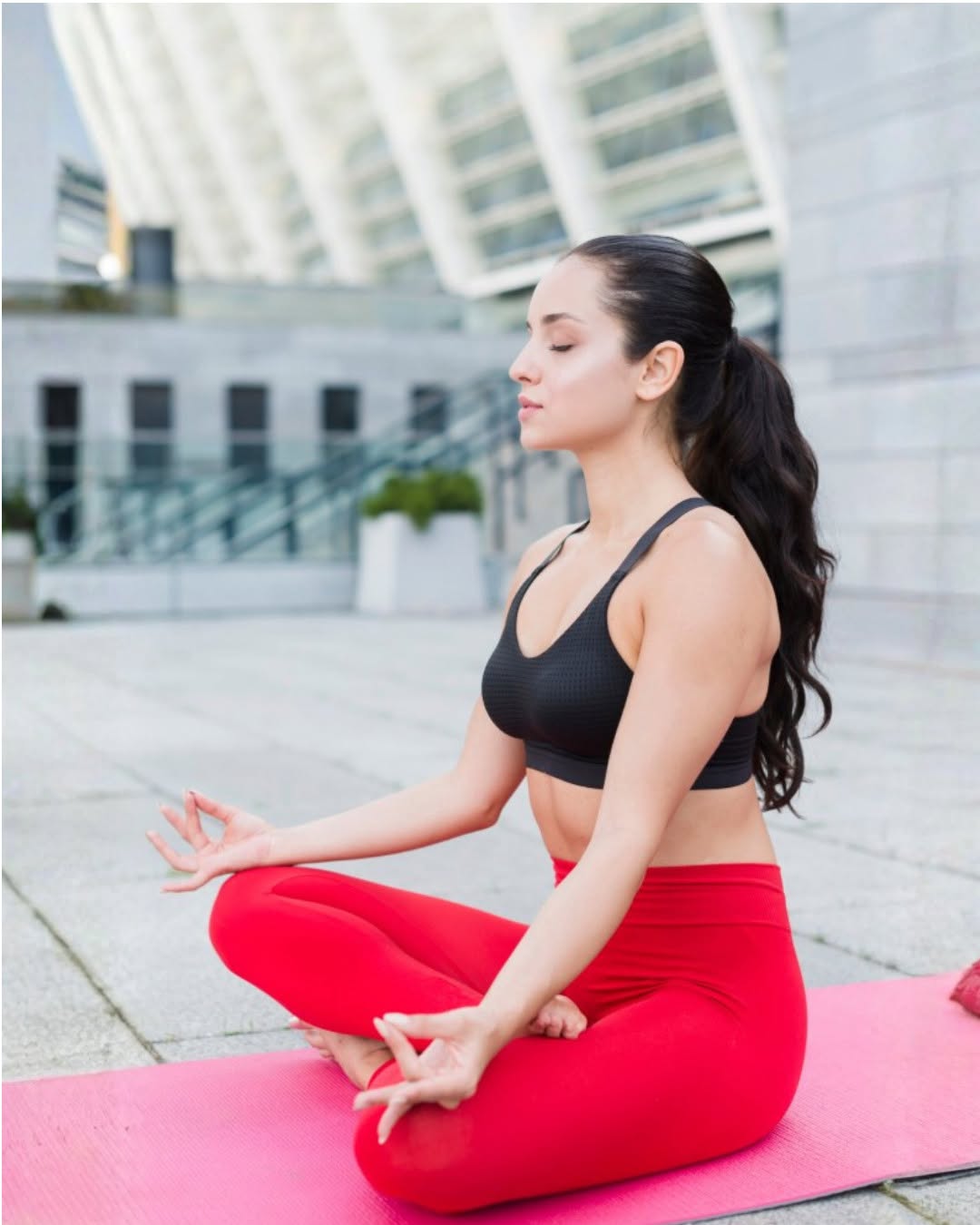 Woman meditating on a pink yoga mat outdoors